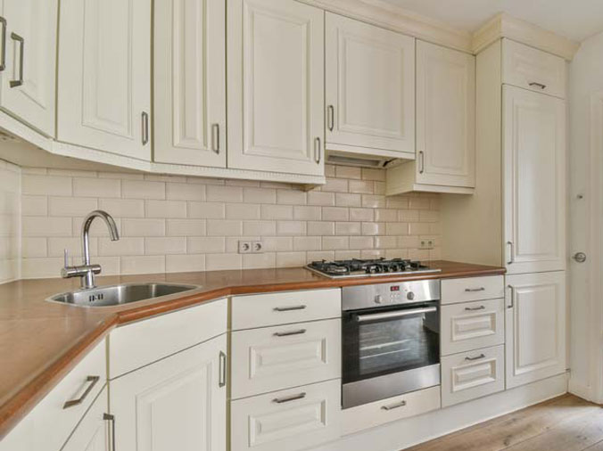 Kitchen with white cabinets, natural wood countertop and stainless sink and hardware